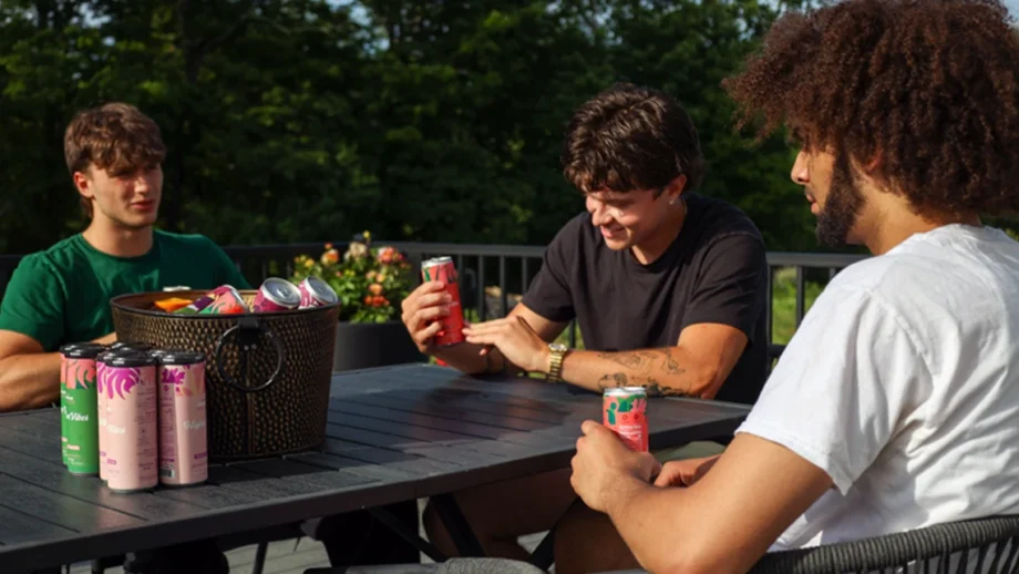 Three friends on a porch holding Wunder weed drinks beside a basket of more THC cans