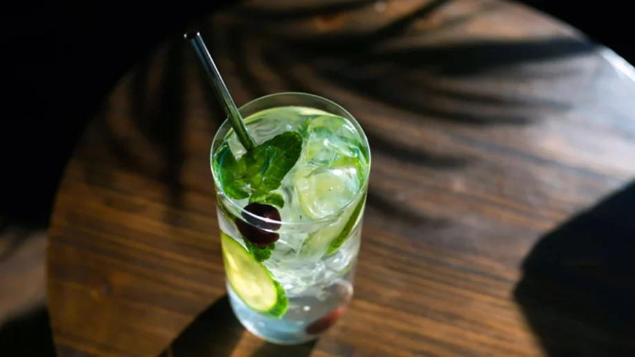 A glass of cannabis-infused spritzer with a straw, ice cubes, mint leaves, and cucumber slices