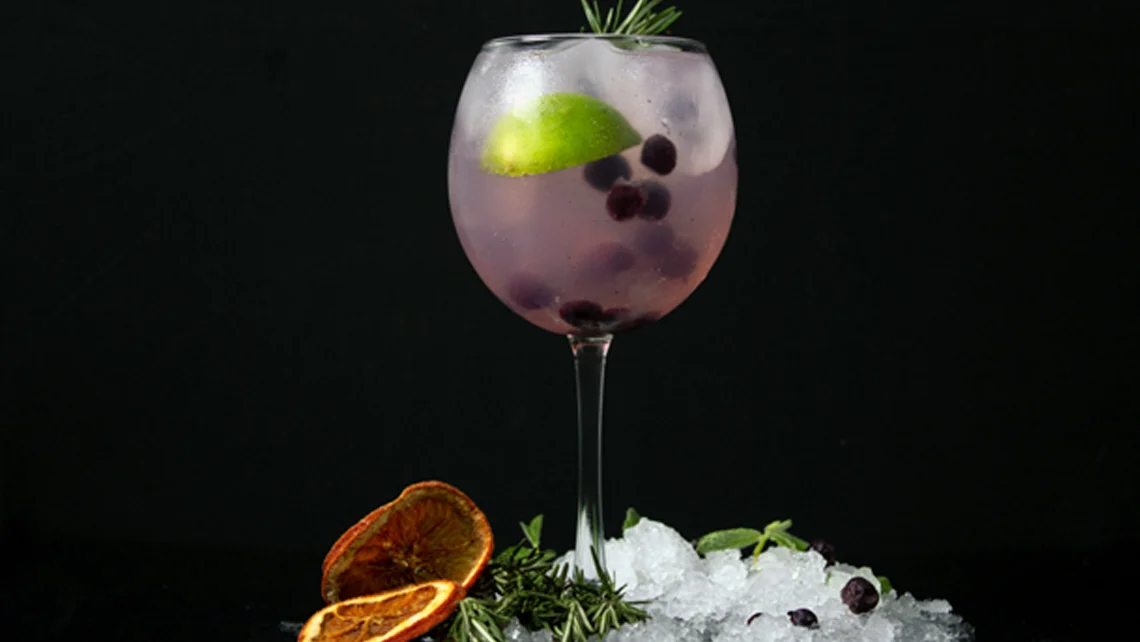 A wine glass of cannabis spritzer with a lime wedge and berries, surrounded by ice and orange slices