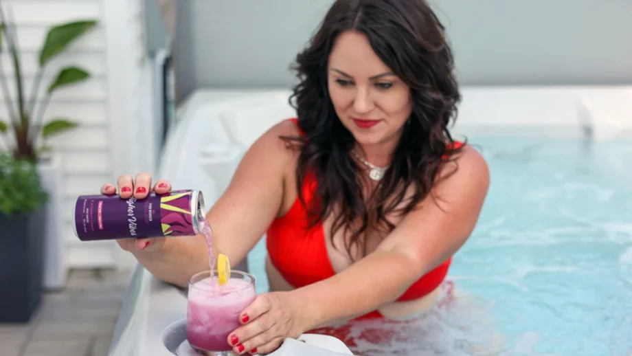 Lady in a jacuzzi tub pouring Wunder Higher Vibes into a glass with ice and lemon slice